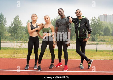 Vier junge freundliche interkulturelle Menschen in Sportkleidung auf Rennstrecke Stockfoto