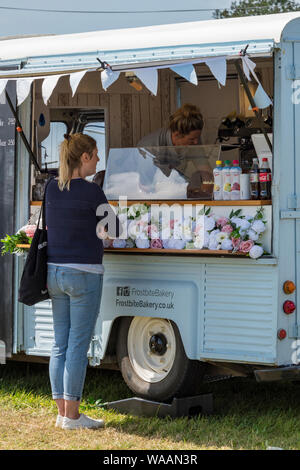 Eine junge Frau, bestellen einen Kaffee aus einer mobile Gastronomie van auf ein Land zeigen. Stockfoto