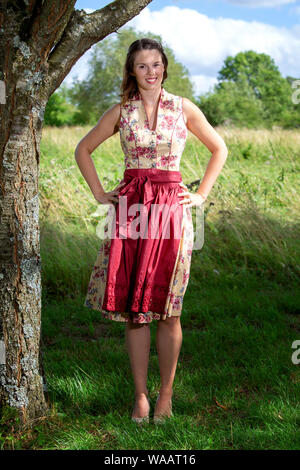 Porträt der jungen Frau im Dirndl durch Baum stehend Stockfoto