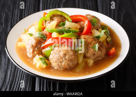 Rezept für zarte Fleischbällchen geschmort mit frischer Ananas und Paprika in süß-saurer Sauce close-up auf einem Teller auf den Tisch. Horizontale Stockfoto