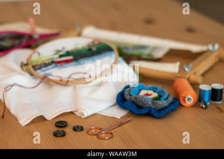 Kreuzstich sticken Materialien, einschließlich Threads, Nadeln, Scheren, Bettwäsche und Bänder. auf einen Tisch für Handwerk und Hobby Stockfoto