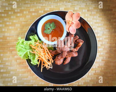 Frittierte Rind- oder Schweinefleisch mit Soße und frisches Gemüse auf dem Teller in den hölzernen Tisch anzeigen/Thai Fried Sonne getrocknetem Rindfleisch asiatisch Essen Stockfoto