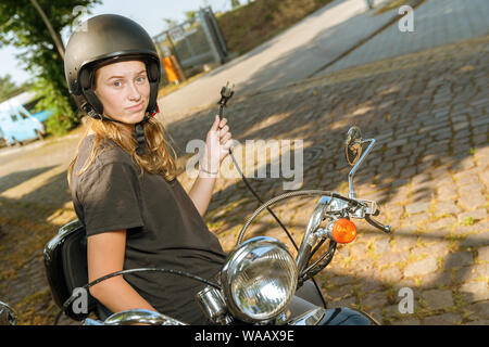 Junge Frau mit einem elektrischen scooter ist auf der Suche nach einer Steckdose zum Aufladen Stockfoto