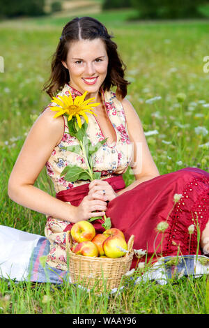 Porträt der jungen Frau im Dirndl sitzen in der Wiese und Sonnenblumen Stockfoto