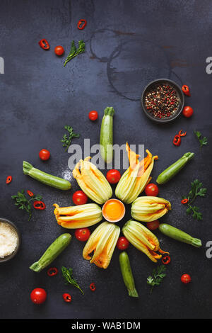 Frisch geernteten Zucchini und Zucchiniblüten auf rustikalen dunklen Tisch, bereit, Zutaten für die Füllung. Ansicht von oben, leeren Raum Stockfoto