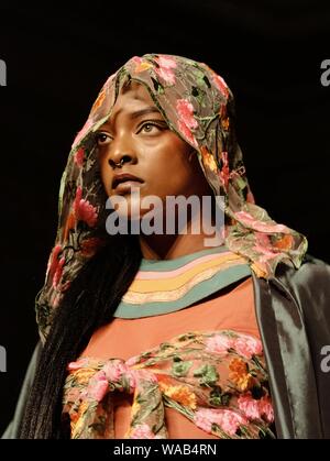 Ein Modell mit einem floralen Kopftuch geht für Designer Muhire während der Africa Fashion Week in London spazieren. Stockfoto