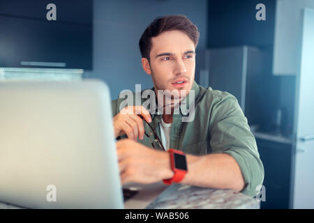 Ernsthaften jungen Mann in der Nähe von Laptop zu Hause sitzen Stockfoto