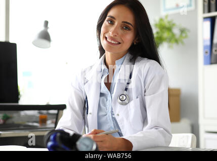 Hübsche reife weibliche GP am Arbeitstisch Notizen zu machen Stockfoto