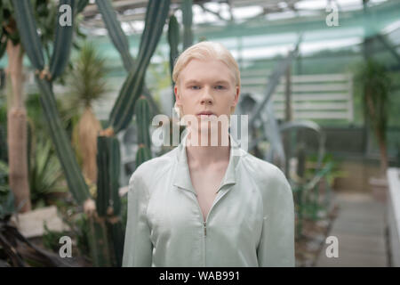 Ernsthafte männliches Modell stehen in der Nähe von Pflanzen im Gewächshaus Stockfoto