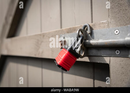 Ein rotes Vorhängeschloss sichern eine Schraube an einem grauen Gartentor. Stockfoto