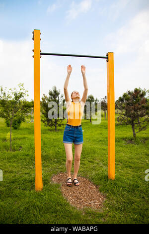 Schöne junge Frau hing auf der horizontalen Leiste. Sport und Leibeserziehung. Eine Blondine in Shorts und ein T-Shirt ist Training im Freien. Stockfoto