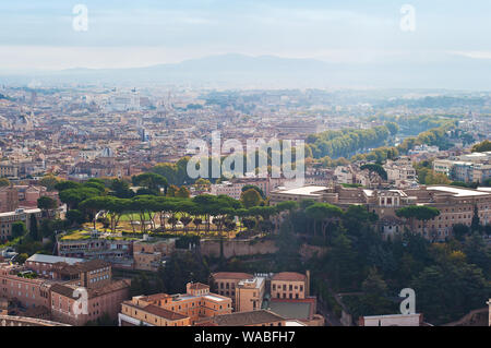 Blick auf viele orange Dächer und Reihen von hohen grünen Bäumen und Umriss eines Smoky Mountain Range, Rom, Italien. Sonnigen Herbsttag. Von oben geschossen Stockfoto