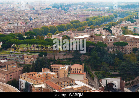 Blick auf viele orange Dächer und Reihen von hohen grünen Bäumen und Umrisse einer rauchigen Skyline, Rom, Italien. Sonnigen Herbsttag. Von oben geschossen Stockfoto