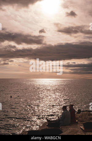 Paar entspannende an der felsigen Küste bei Sonnenuntergang, Rovinj, Istrien, Kroatien Stockfoto