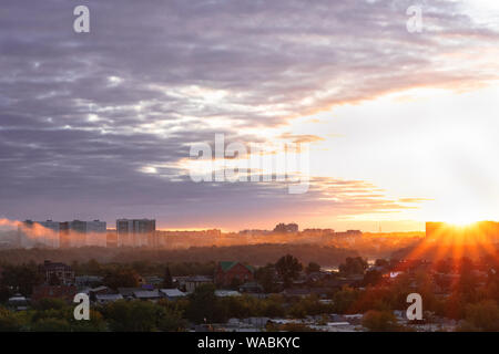 Der Himmel über der Stadt bei Sonnenuntergang. die Sonnenstrahlen durch dicke Wolken. orange, gelb, rosa Reflexionen. Mehrfarbige Nebel oder Dunst über der Stadt. Stockfoto