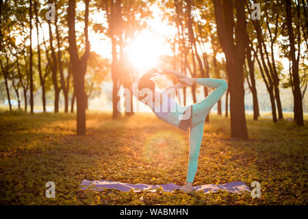 Dünne brünette Mädchen tun Natarajasana übung, Herr des Tanzes pose im Herbst Park auf einen Sonnenuntergang Hintergrund. Frau Übungen auf der Yogamatte. Ein Stockfoto