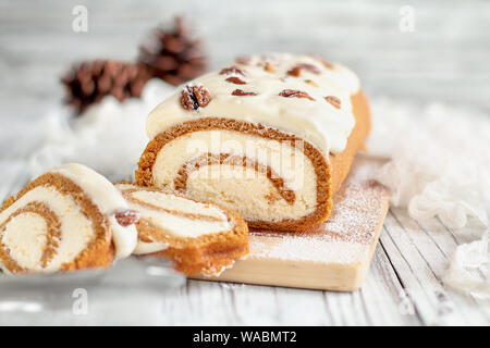 Schöne frische gebackene pumpkin Spice roll Kuchen mit Puderzucker, Pekannüsse, Frischkäse füllen und Vereisung. Extreme selektiven Fokus mit Backgr verschwommen Stockfoto