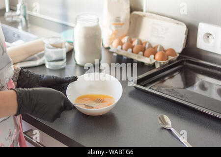 Frau Hände schlagen, Eier in einer Schüssel mit einer Gabel. Prozess der schlagenden Eier. Zutaten zum Backen: Mehl, Eier, Milch, Zucker. Stockfoto