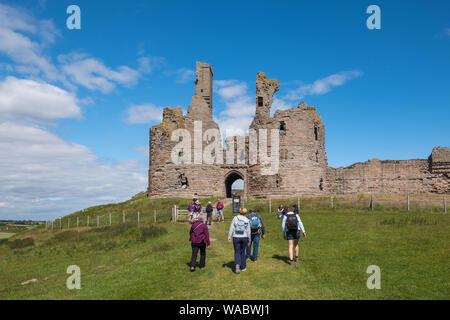 Gruppe der Wanderer zu Fuß in Richtung Dunstanburgh Castle in der Nähe von Alnwick an der Küste von Northumberland, Großbritannien Stockfoto