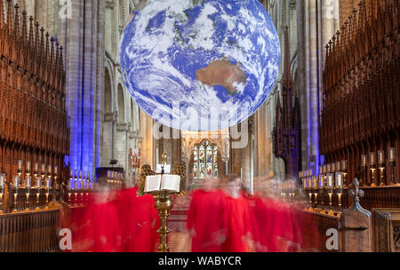 Choristen kommen für evensong als Gaia, ein 23 ft Replik des Planeten Erde hängt, auf der Kathedrale von Peterborough. Stockfoto