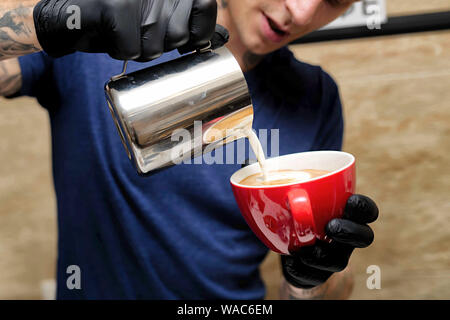 7/8 shot der weiblichen Barista eine Tasse Kaffee steht hinter cafe Zähler. Junge Frau gießen Milch in eine Tasse Kaffee. Stockfoto