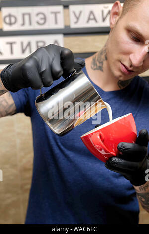 7/8 shot der weiblichen Barista eine Tasse Kaffee steht hinter cafe Zähler. Junge Frau gießen Milch in eine Tasse Kaffee. Stockfoto