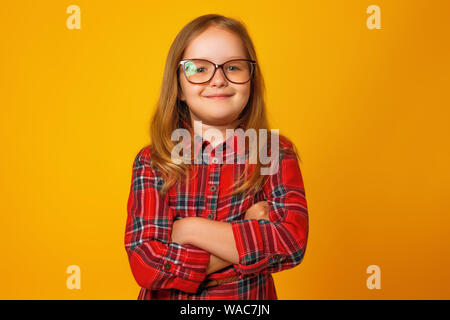 Porträt eines kleinen blonden Mädchen im roten Kleid auf einem gelben Hintergrund. Das Kind steht in Gläser mit verschränkten Armen. Stockfoto