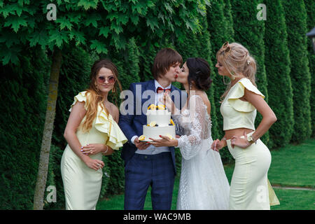 Brautpaare und Brautjungfern Spaß haben und Hochzeitstorte zusammen Essen an der frischen Luft auf Hochzeit. Stockfoto