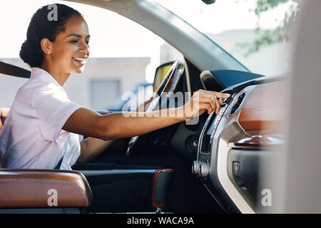 Lächelnde Frau Einstellknopf am Armaturenbrett. Happy businnesswoman in einem Auto sitzen und über die Navigation. Stockfoto