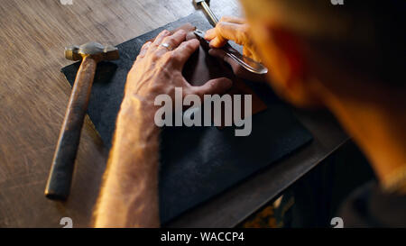 Verarbeitung von Leder Los in der Werkstatt. Mann hält crafting Tool und Arbeiten. Handwerker in der Gerberei. Stockfoto