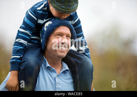 Lächelnd im mittleren Alter Mann seinem jungen Sohn auf seine Schultern. Stockfoto