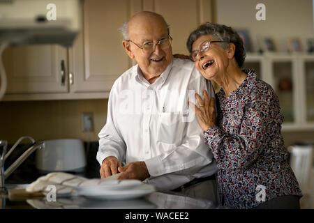 Lächelnde ältere Paare teilen ein liebevoller Moment, während sie das Geschirr zusammen tun. Stockfoto