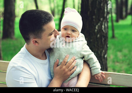 Ein Jahr altes Mädchen in die Arme ihres Vaters auf der Straße, der Frühling. Vater geht mit dem Kind. Erste Schritte der Tochter Stockfoto