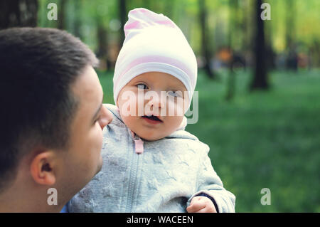 Ein Jahr altes Mädchen in die Arme ihres Vaters auf der Straße, der Frühling. Vater geht mit dem Kind. Erste Schritte der Tochter Stockfoto