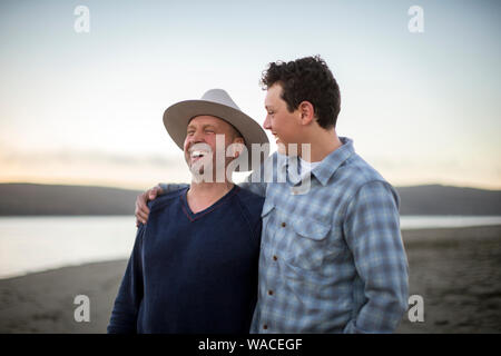 Teenager und sein Vater gemeinsam lachen am Strand bei Sonnenuntergang. Stockfoto