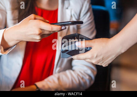 Closeup Porträt der jungen Frau sitzt mit mobilen Smart Phone und Zahlung per Pay pass pos. kontaktlosen NFC-Technologie auf Handy und Zahlung conce Stockfoto