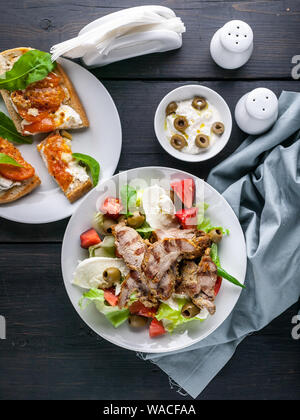 Salat mit Gemüse, Kräuter und Mozzarella. Gebratenes Fleisch. Panini, Sandwiches mit Käse, Tomaten und Rucola. Traditionelle mediterrane Küche Stockfoto