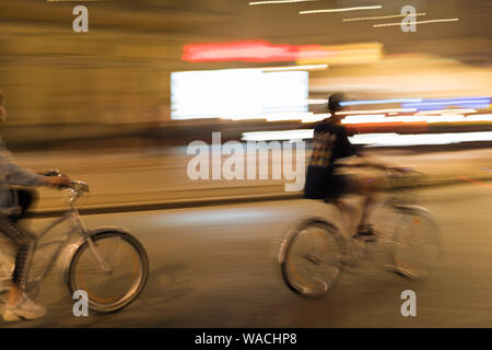 Zwei junge Leute fahren mit dem Fahrrad durch die Stadt bei Nacht Stockfoto