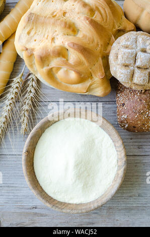 Verschiedene Arten von traditionellen Italienischen frisch gebackenes Brot und Brötchen mit Schüssel Mehl auf hölzernen Tisch Hintergrund. Rustikale Vintage Style. Ansicht von oben. Stockfoto