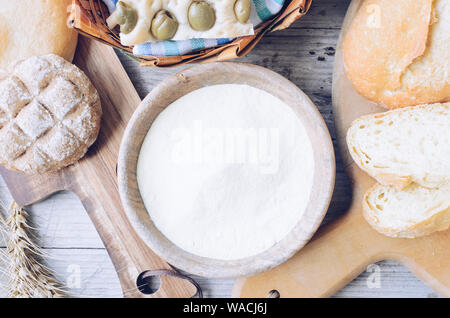 Verschiedene Arten von traditionellen Italienischen frisch gebackenes Brot und Brötchen mit Schüssel Mehl auf hölzernen Tisch Hintergrund. Rustikale Vintage Style. Ansicht von oben. Stockfoto