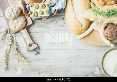 Verschiedene Arten von traditionellen Italienischen frisch gebackenes Brot und Brötchen mit Schüssel Mehl auf hölzernen Tisch Hintergrund. Rustikale Vintage Style. Ansicht von oben. Co Stockfoto