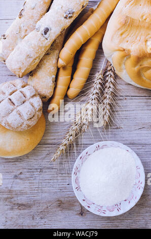 Verschiedene Arten von traditionellen Italienischen frisch gebackenes Brot und Brötchen mit Schüssel Mehl auf hölzernen Tisch Hintergrund. Rustikale Vintage Style. Ansicht von oben. Stockfoto