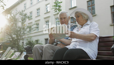Älteren zwei männliche und weibliche Touristen sitzt auf der Bank im Stadtzentrum mit einer Karte in der Hand und auf der Suche nach der Route während in Lviv, Ukraine reisen. Elegante Frau in hat. Familienurlaub Konzept Stockfoto