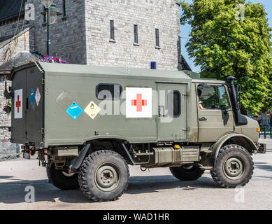 Han-sur-Lesse, Belgien - 25. Juni 2019: Belgische Armee grün ambulance Truck mit rotem Kreuz symbol Innenstadt und grünem Laub. Grau Gebäude aus Stein in Ba Stockfoto