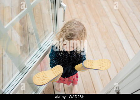 Mädchen in der Tür stehen mit Blick auf den regen Stiefel auf ihre Hände Stockfoto