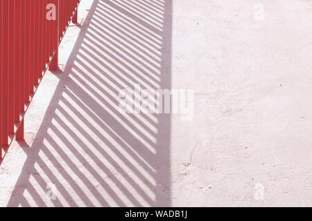 Orange Rot Geländer werfen Schatten über eine reine Betonboden. Viele gerade Linien führen die Zusammensetzung. Stockfoto