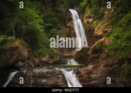 Wandern Frau in Rot Jacke Aufenthalt im großen Wasserfall in den Bergen. Stockfoto