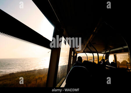 Passagier aus einem Bus-Fenster auf dem oberen Deck des Abends die Sonne über dem Meer Stockfoto