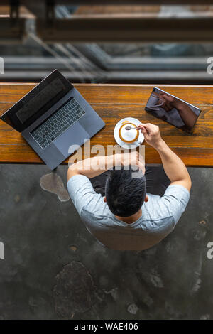 Vertikal oben anzeigen Foto der Asiatischen Freiberufler seinen Kaffee genießen. Stockfoto
