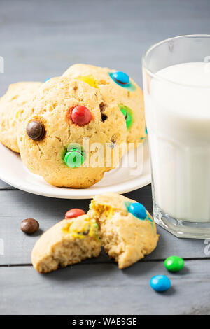 Ein Glas Milch und hausgemachte Kekse mit bunten Jelly Beans Süßigkeiten eingerichtet. Kinder Frühstück Snack. Vertikale Rahmen Stockfoto